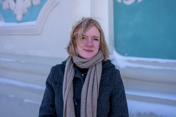 Erika Fatland med vindblåst blondt hår og beige skjerf foran en turkis og hvit barokkfasade i snø i Ukraina